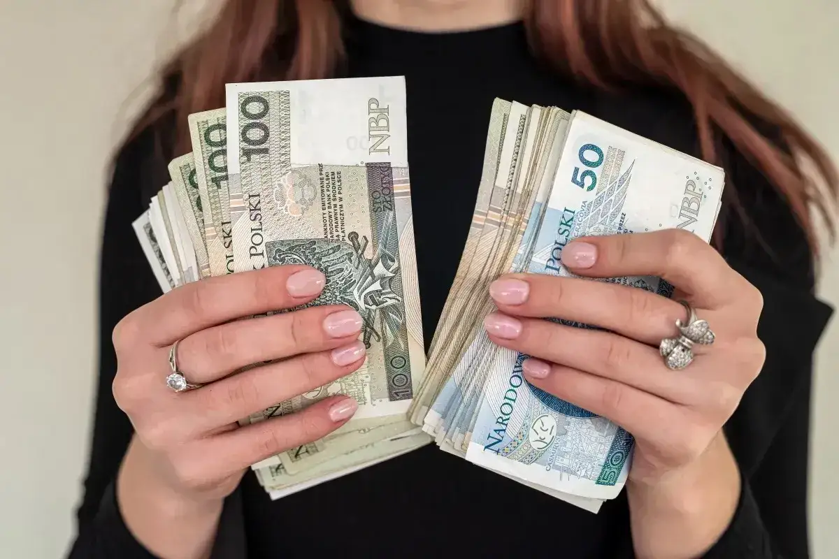Dłonie trzymające stosy polskich banknotów 100 zł i 50 zł. Marzysz, jak zarobić dużo pieniędzy? Oto inspiracja!