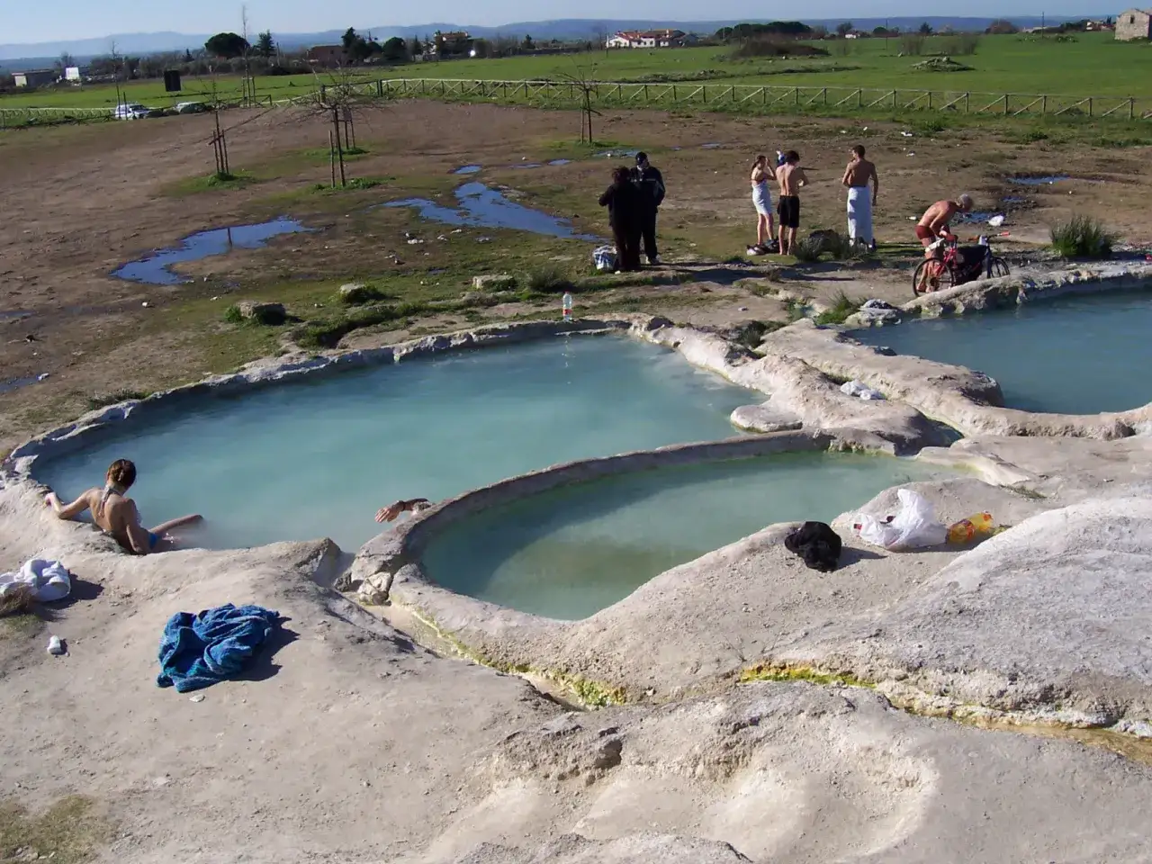 Bagni termali naturali nella Tuscia, con persone che si rilassano nelle acque azzurre e un ciclista.