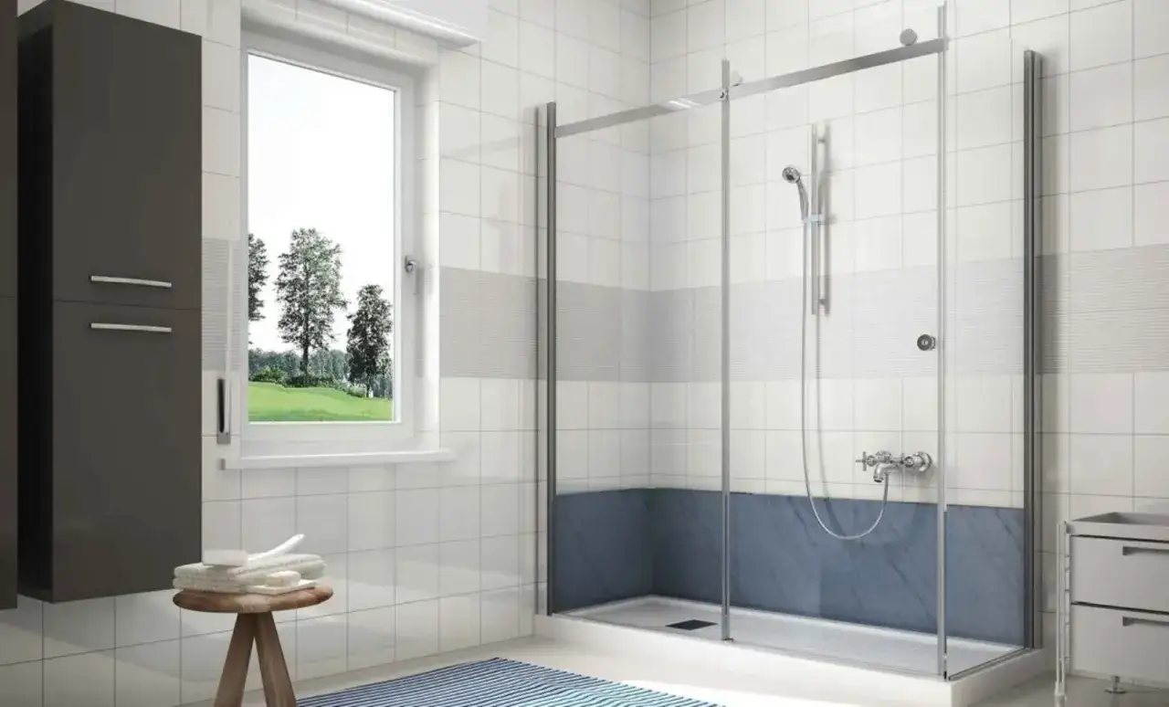 Idee per come abbellire un bagno fai da te: doccia moderna, mobile scuro, finestra con vista verde e sgabello con asciugamani.