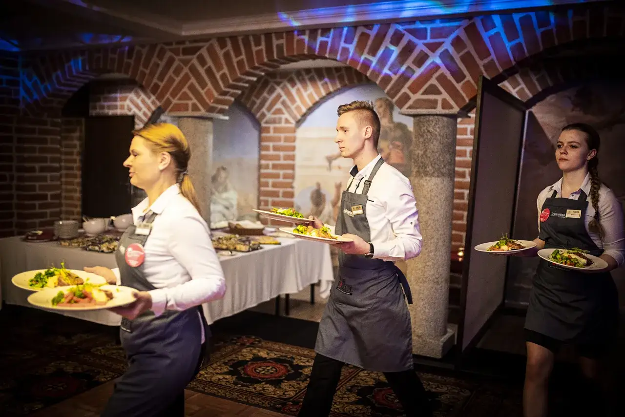 Kelnerzy niosą talerze z jedzeniem. Zastanawiasz się, jak się ubrać na kolację all inclusive? Elegancko, ale wygodnie.
