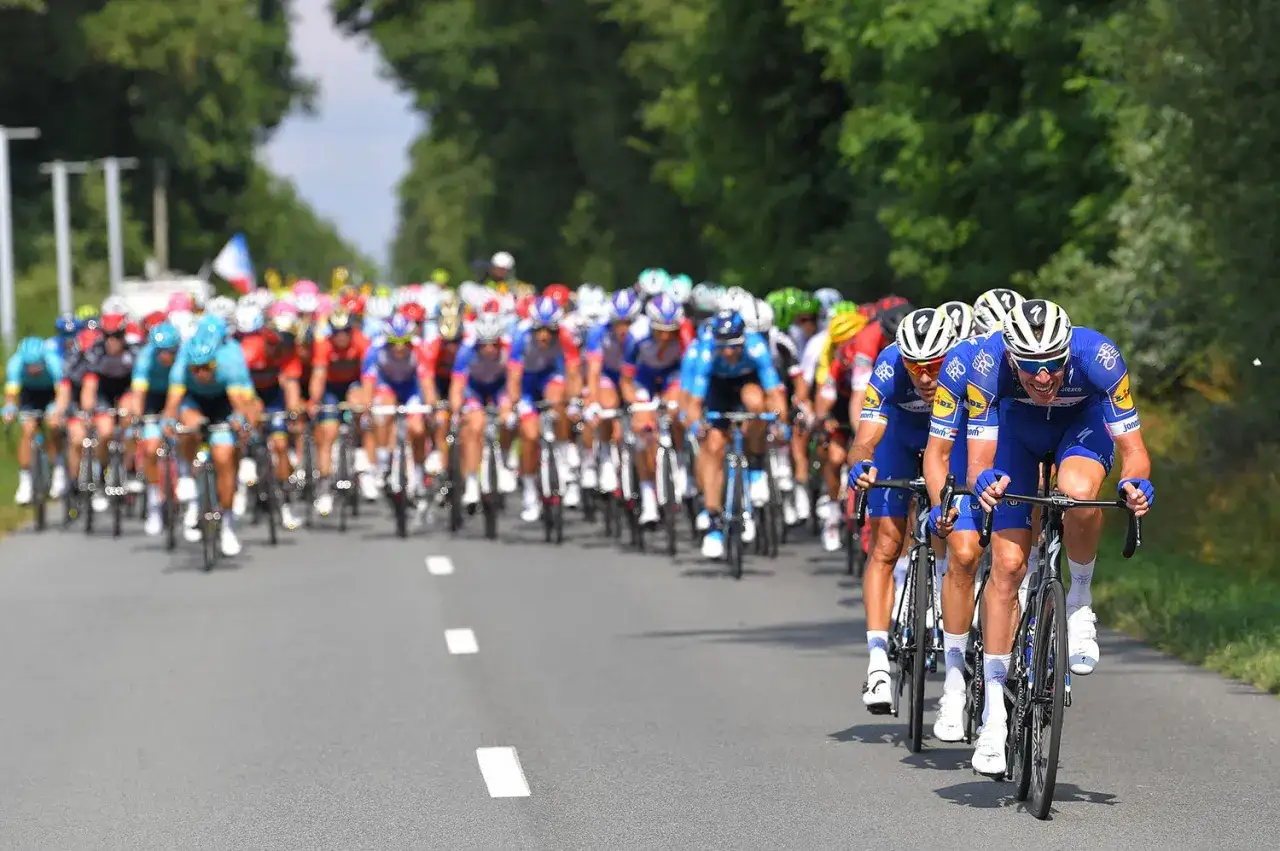 Radfahrer in blauen Trikots, Teil der Tour de France Teams, kämpfen auf der Straße um die Führung.
