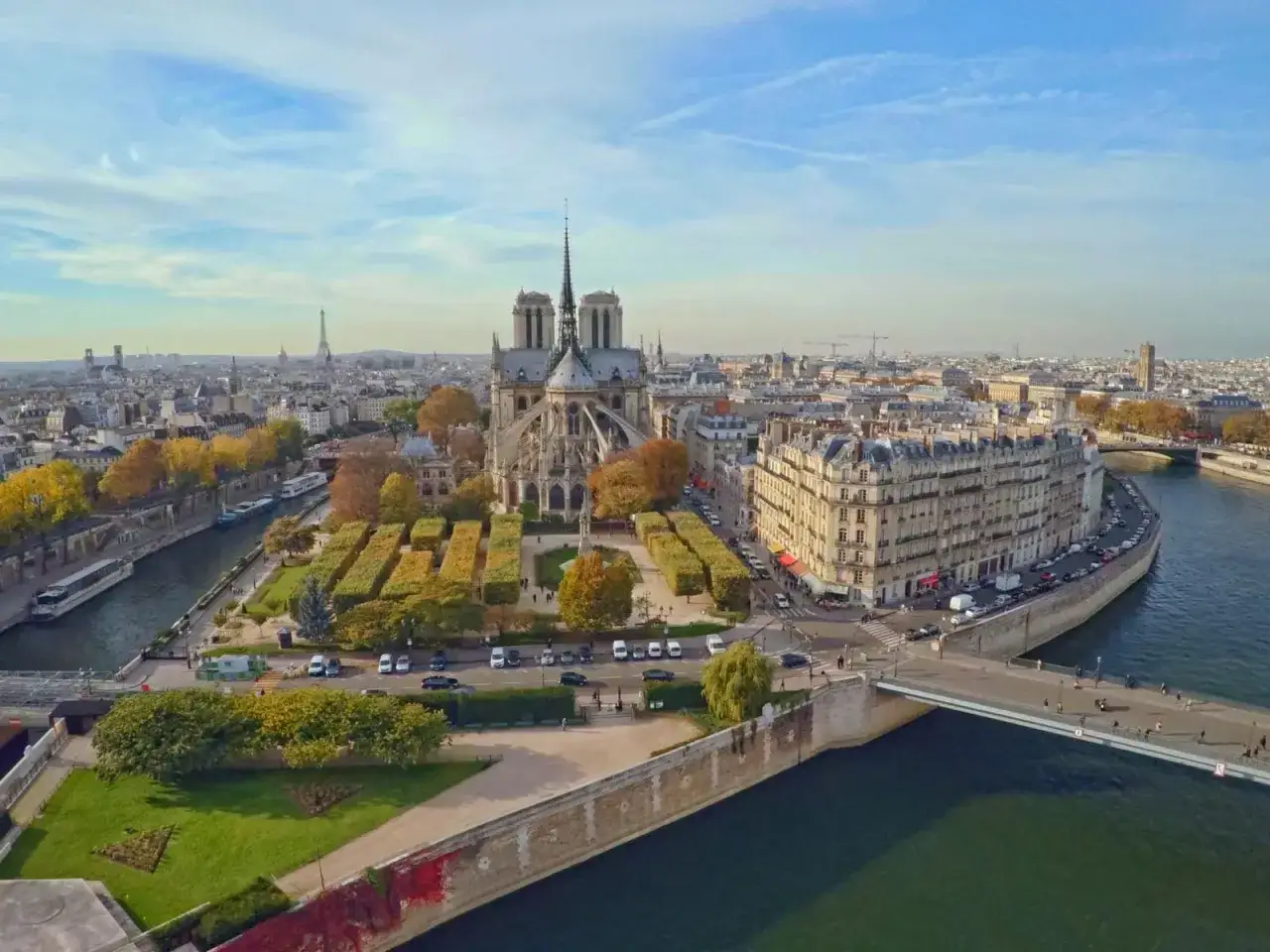 Vista aérea de la Île de la Cité en París, con la majestuosa Catedral de Notre Dame en el centro, rodeada de árboles otoñales y el río Sena.