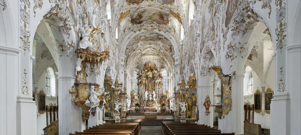 Prunkvolle Kirche mit Stuck und Fresken, die Szenen aus dem Leben Marias Geburt darstellen. Goldene Verzierungen und Skulpturen schmücken den Raum.