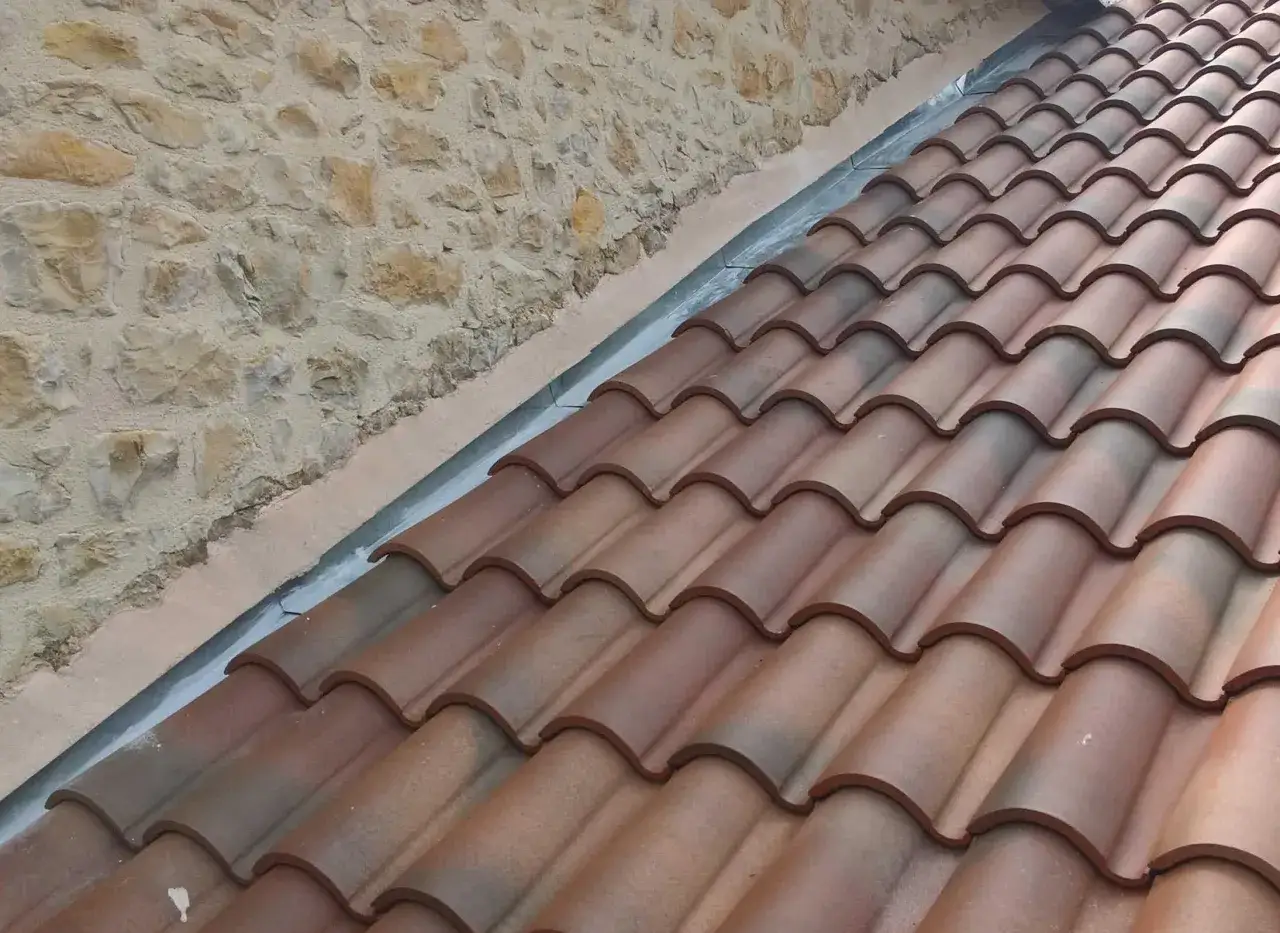 Pose d'un solin en zinc contre un mur en pierre, prot&eacute;geant la jonction avec les tuiles de toiture.