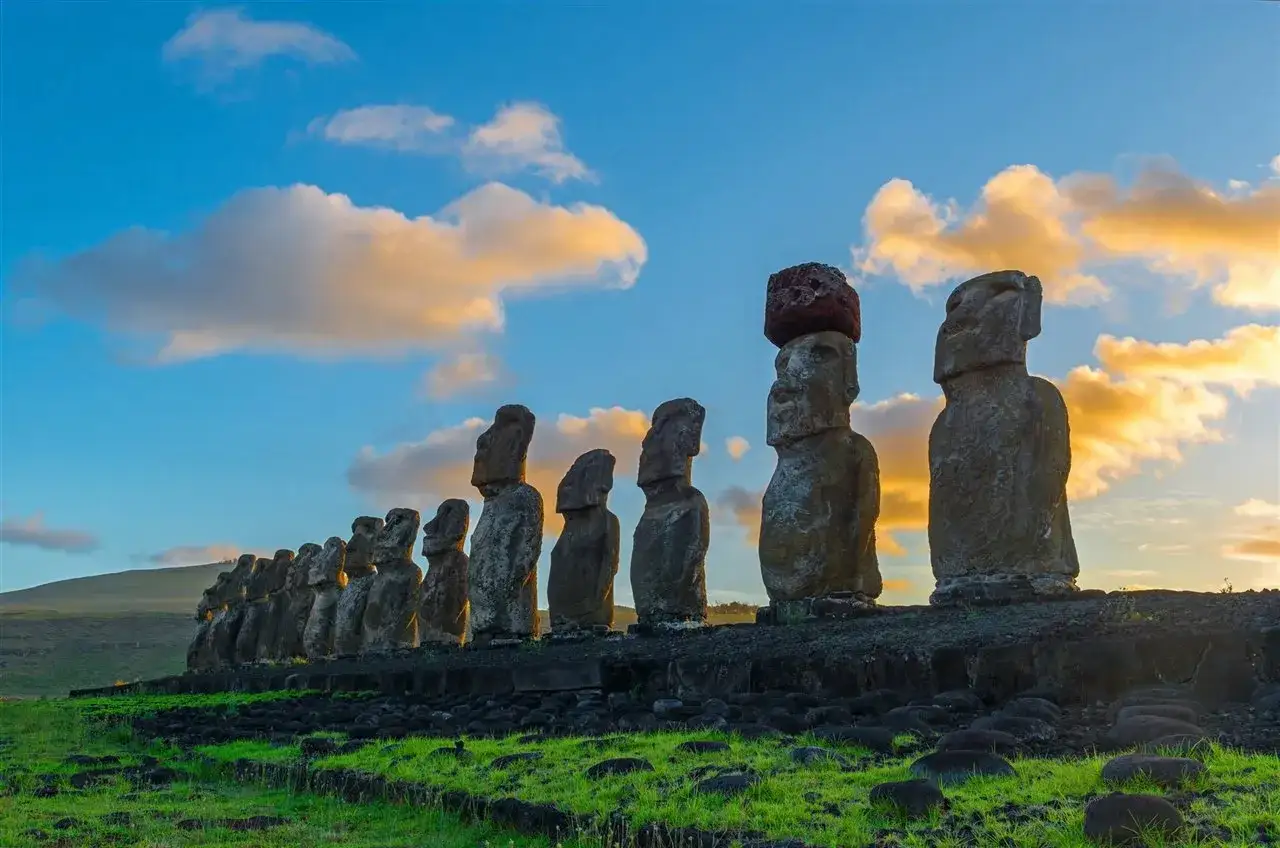 Imponentes moais de la Isla de Pascua se alinean bajo un cielo azul y naranja.