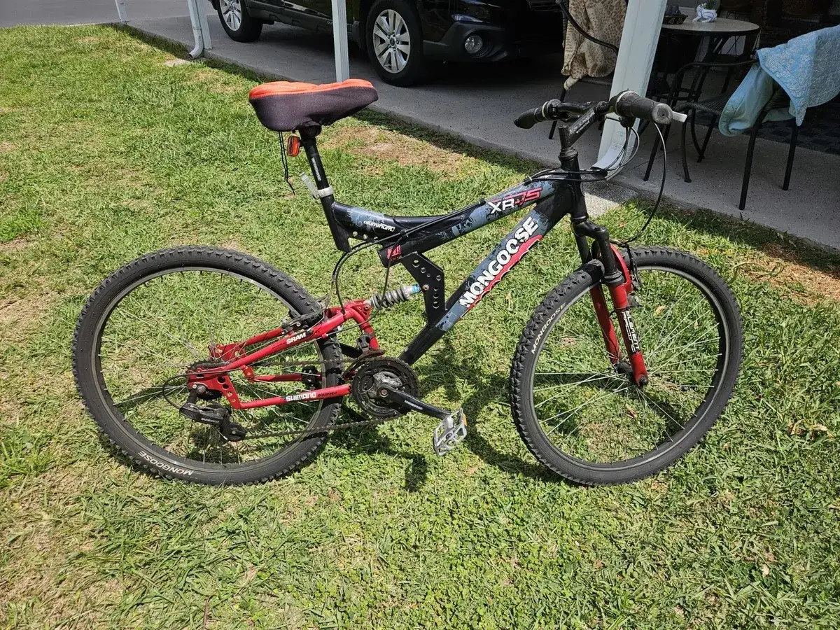 A black and red Mongoose XR-75 full-suspension mountain bike rests on a grassy lawn, ready for its next adventure.