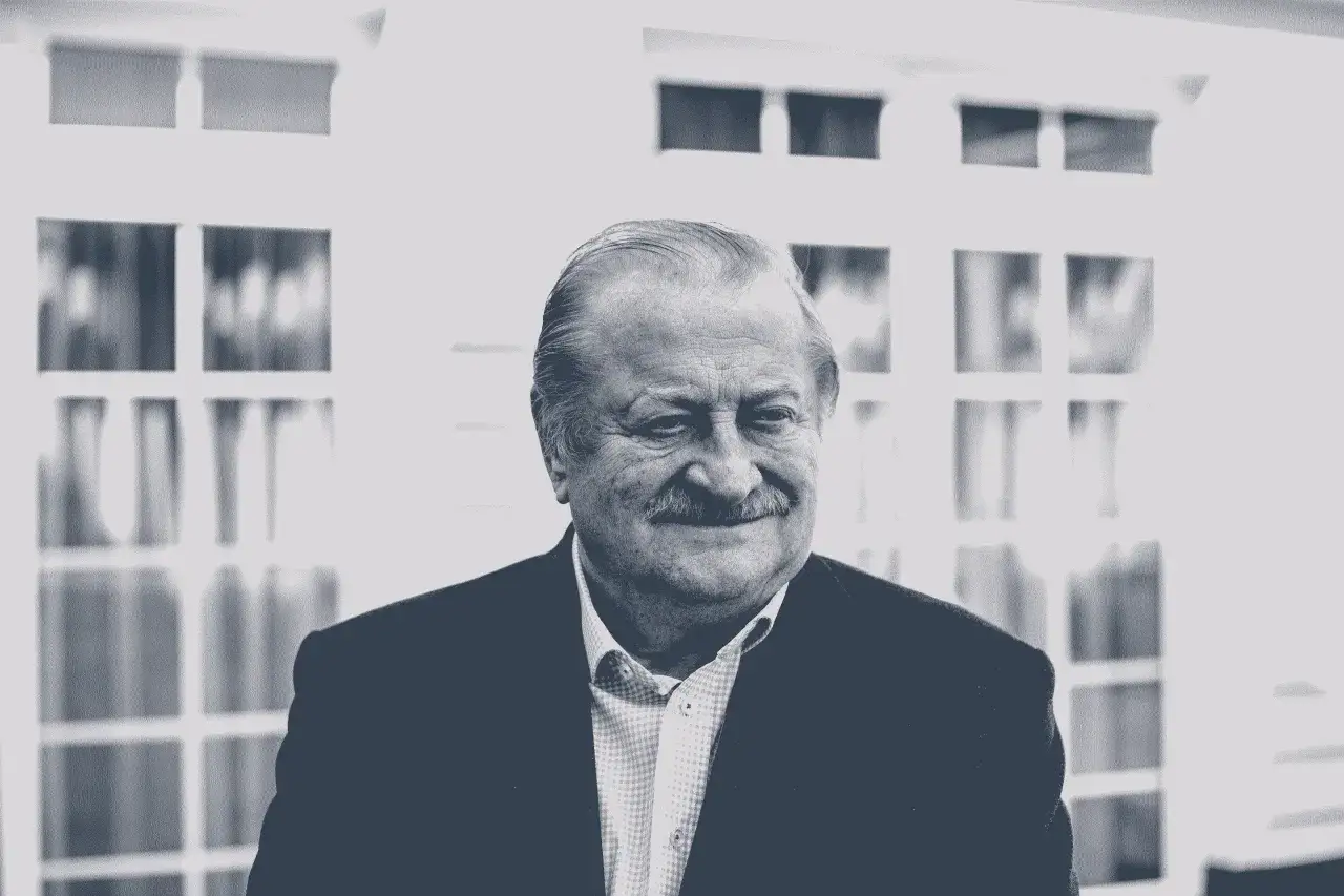 Uśmiechnięty mężczyzna, Jarosław Gołębiewski, w marynarce i koszuli, na tle okien.