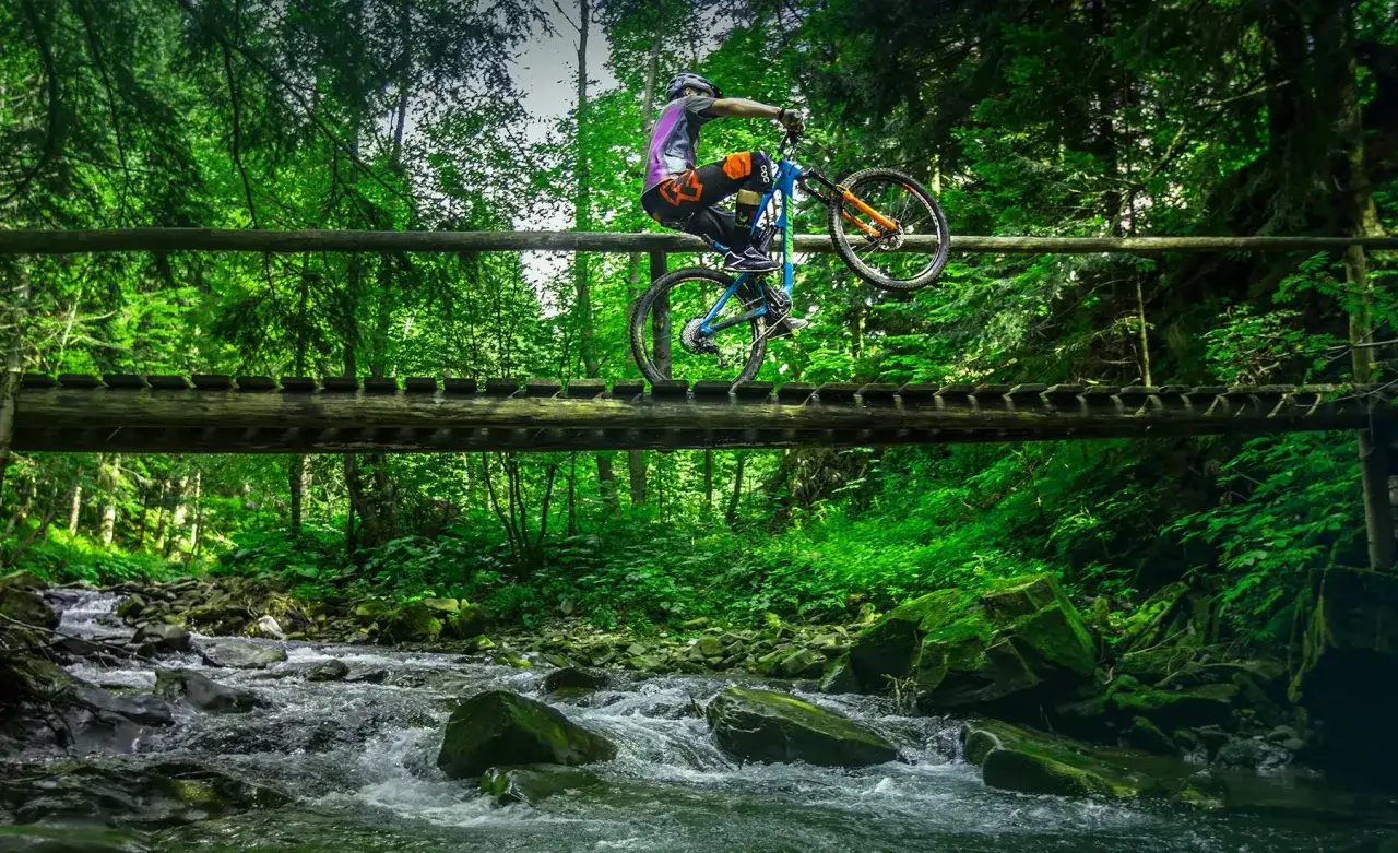 Rowerzysta wykonuje trik na drewnianym moście nad potokiem. Wspaniałe trasy rowerowe Zakopane czekają na odkrycie!