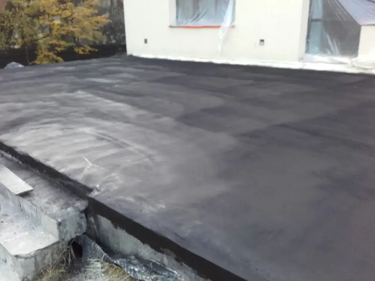 Nowy, ciemny materiał na balkonie, gotowy na fugę. W tle dom z oknami okrytymi folią.
