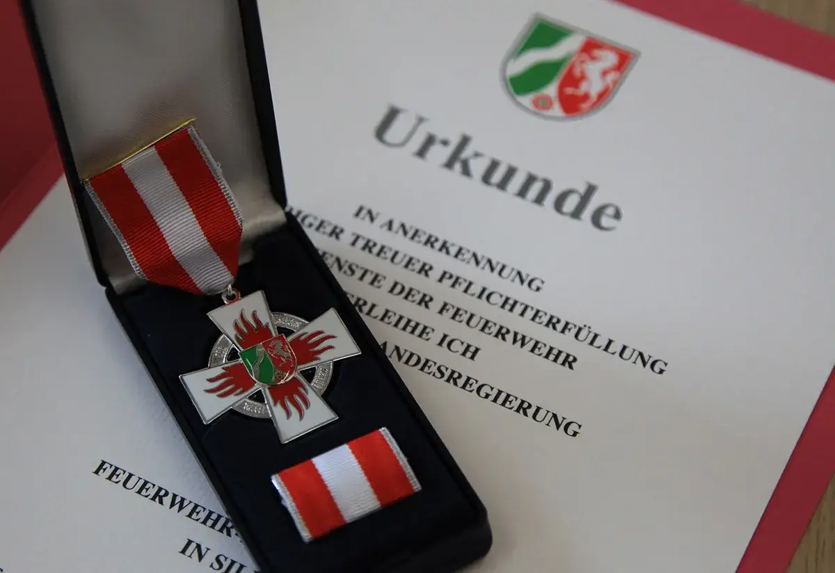 Feuerwehr Ehrenzeichen in einer Schatulle, daneben eine Urkunde f&uuml;r treue Pflichterf&uuml;llung bei der Feuerwehr.
