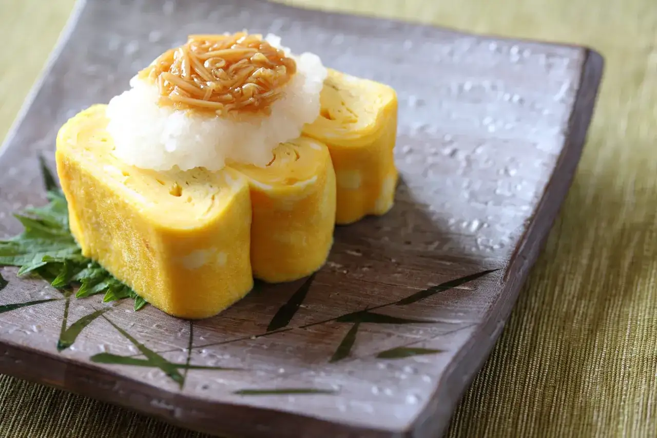 Tamago przepis: zwinięte omlety jajeczne z tartą rzodkiewką i grzybami enoki na talerzu.
