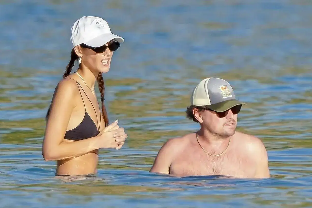 Para się relaksuje, a jego towarzyszka, która mogłaby być jego żoną, w czarnym bikini i białej czapce, cieszy się słońcem.
