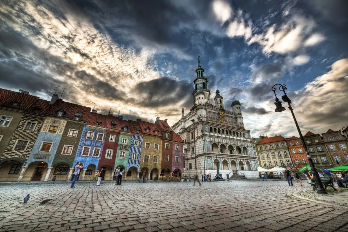 Kolorowe kamienice i renesansowy ratusz na poznańskim rynku pod burzliwym niebem.