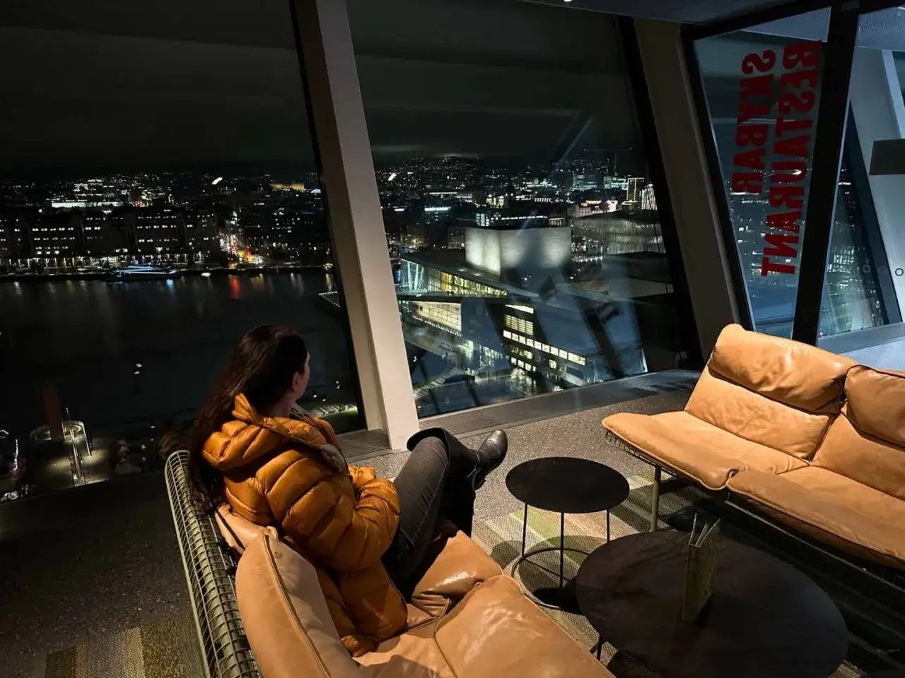 Frau genie&szlig;t den n&auml;chtlichen Ausblick auf Oslo von einem Skybar-Restaurant. Ein perfekter Moment f&uuml;r Oslo Sightseeing.