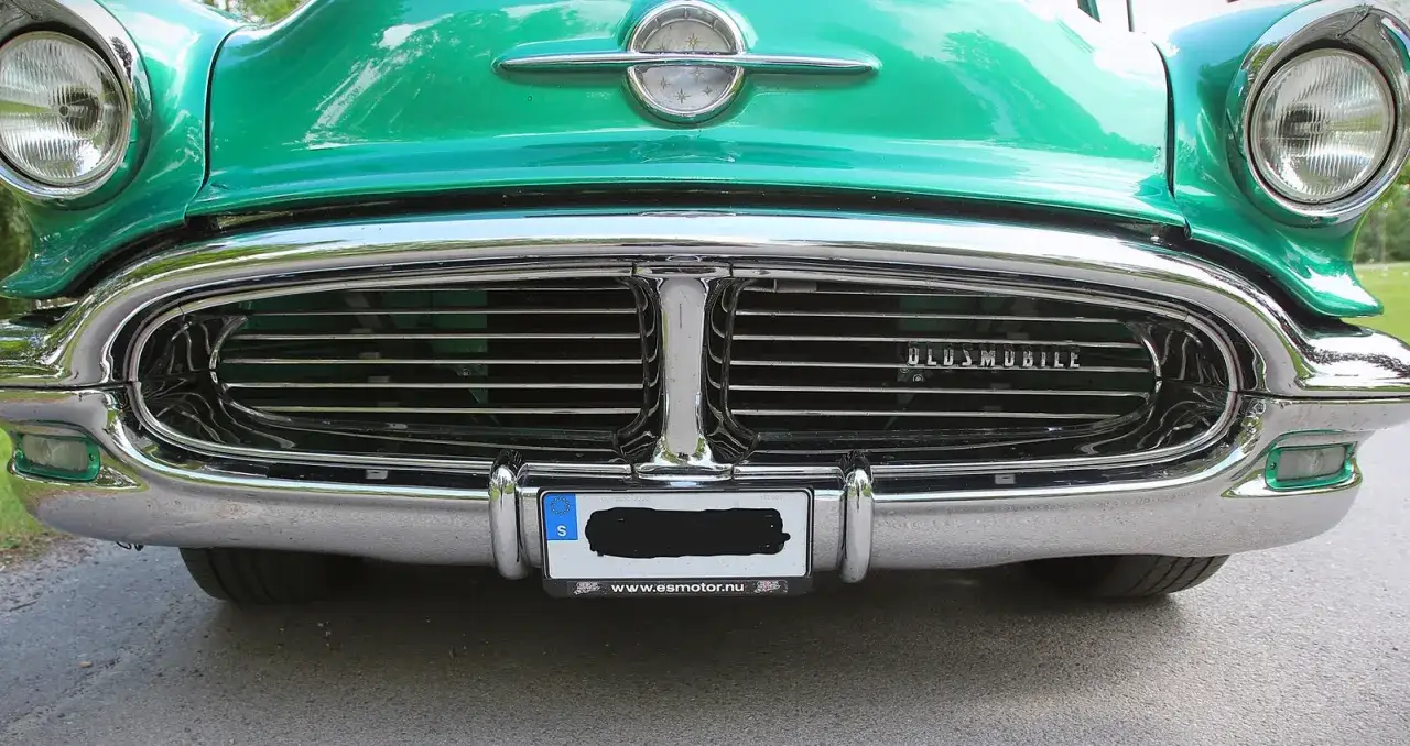 En gl&auml;nsande gr&ouml;n Oldsmobile 1955 med kromdetaljer och en imponerande grill.