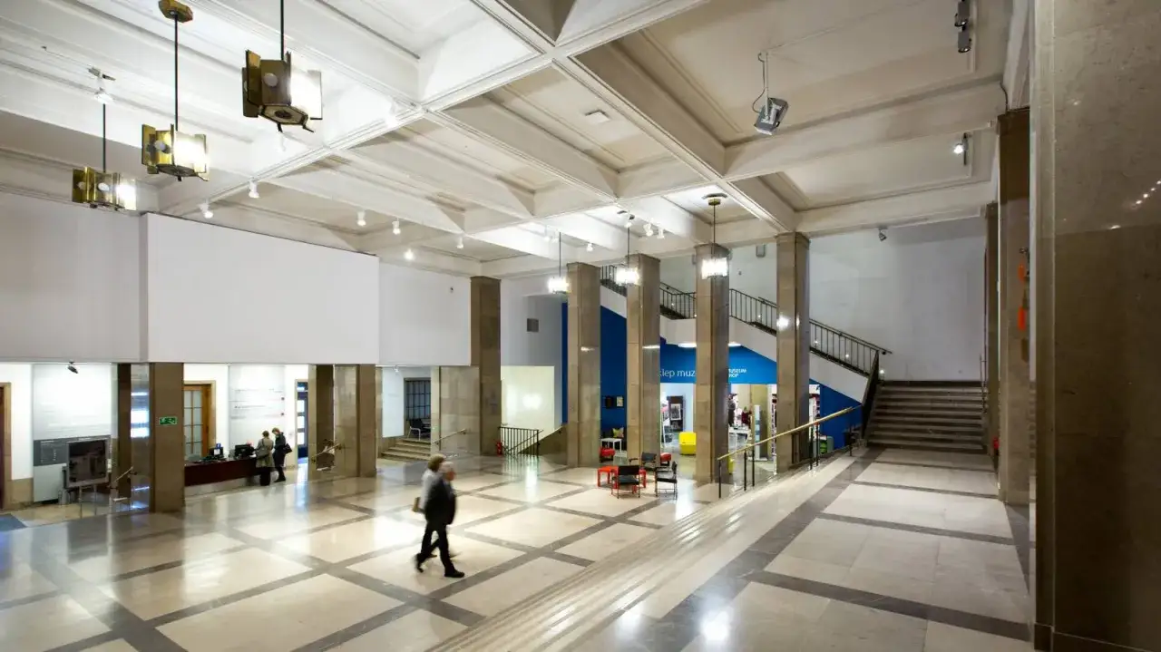 Przestronne wnętrze Muzeum Narodowego w Krakowie przy Alei 3 Maja. Marmurowe kolumny, jasna posadzka i modernistyczne lampy tworzą elegancką atmosferę.