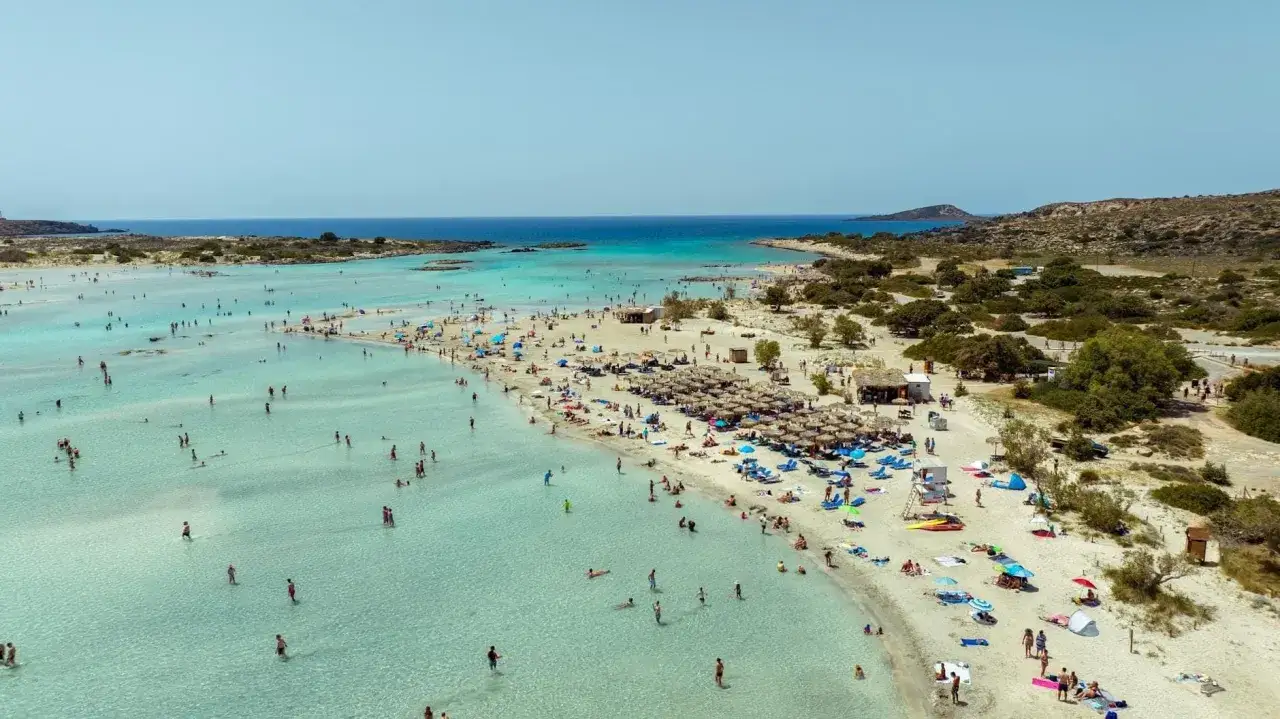 Słoneczna Kreta w sierpniu. Tłumy ludzi cieszą się krystalicznie czystą wodą i piaszczystą plażą.