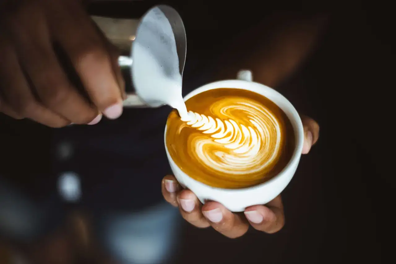 Barista skapar vacker latte art med mjölkskum i en vit kopp.