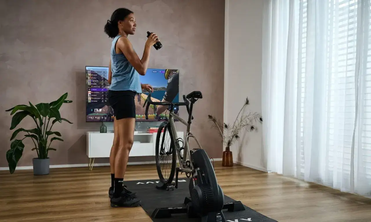 Kobieta pije wodę po treningu na rowerku stacjonarnym. Czy rowerek stacjonarny odchudza brzuch? Regularne ćwiczenia pomagają w redukcji tkanki tłuszczowej.