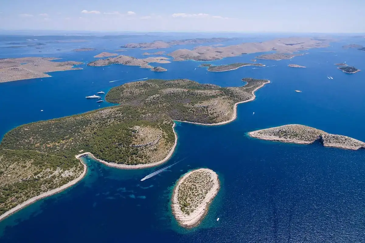 Archipelag wysp w **parku narodowym Kornati** z turkusową wodą i zielonymi wzgórzami. Widoczne łodzie i jachty.