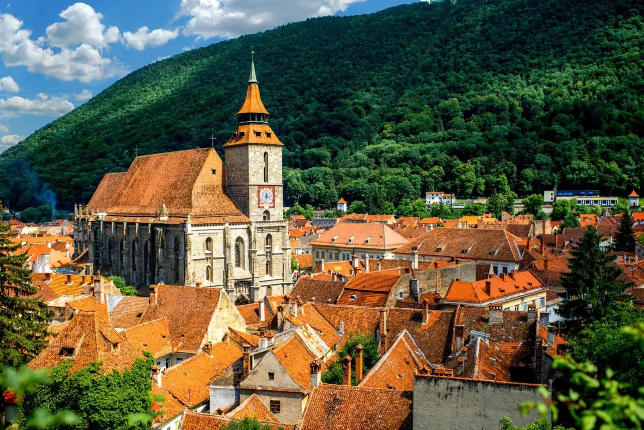 Czarny Kościół w Braszowie, Rumunia, góruje nad miastem z pomarańczowymi dachami, otoczony zielonymi wzgórzami.