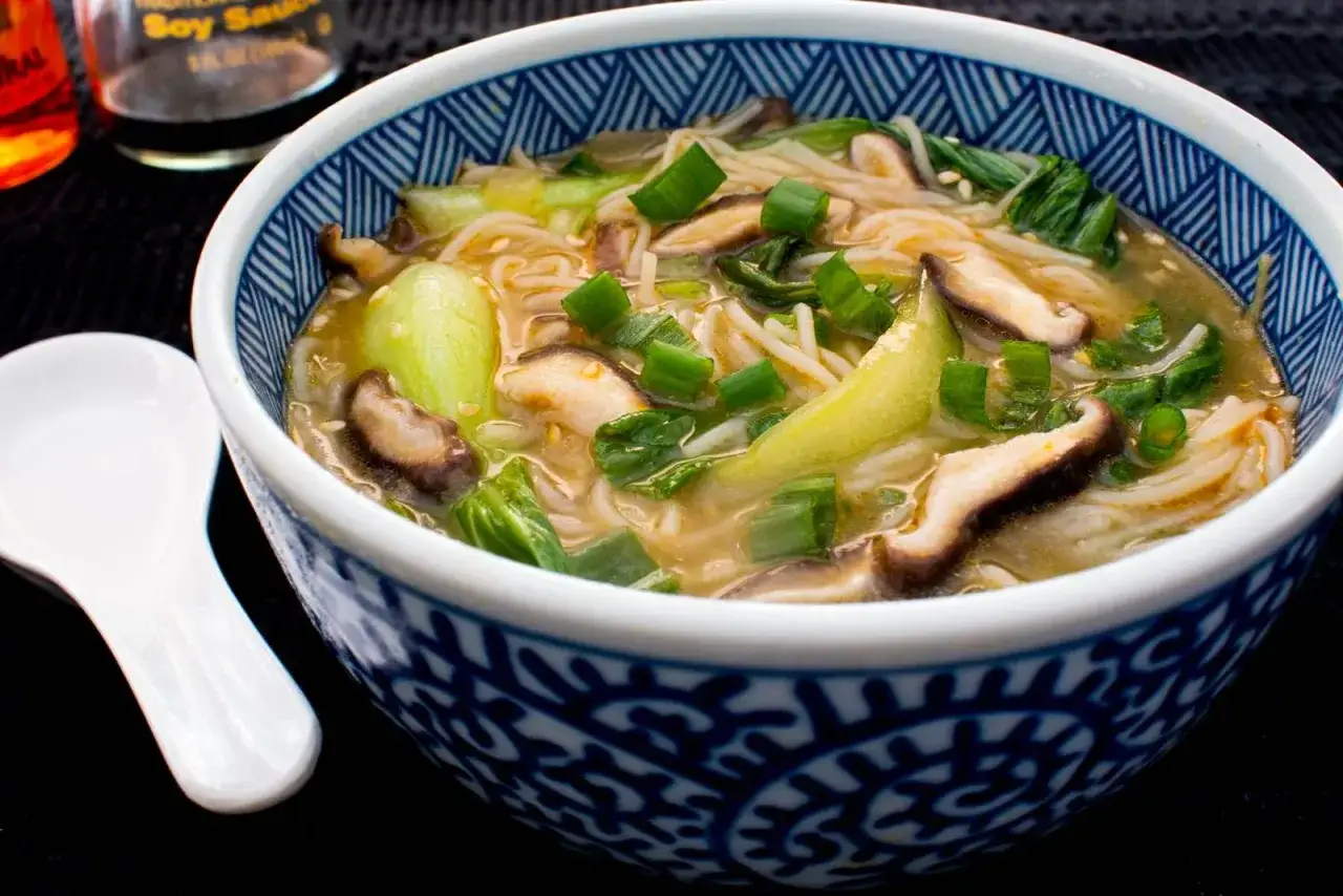 Eine dampfende Sch&uuml;ssel mit Pak Choi Suppe, garniert mit Fr&uuml;hlingszwiebeln und Shiitake-Pilzen.