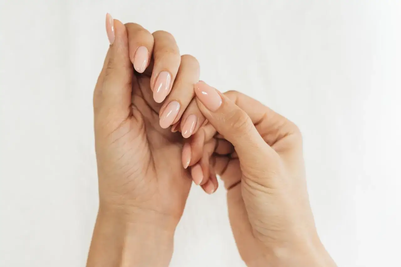 Dłonie z idealnym manicure, pokazujące jak zmiękczyć skórki. Delikatny różowy lakier podkreśla zadbane paznokcie.