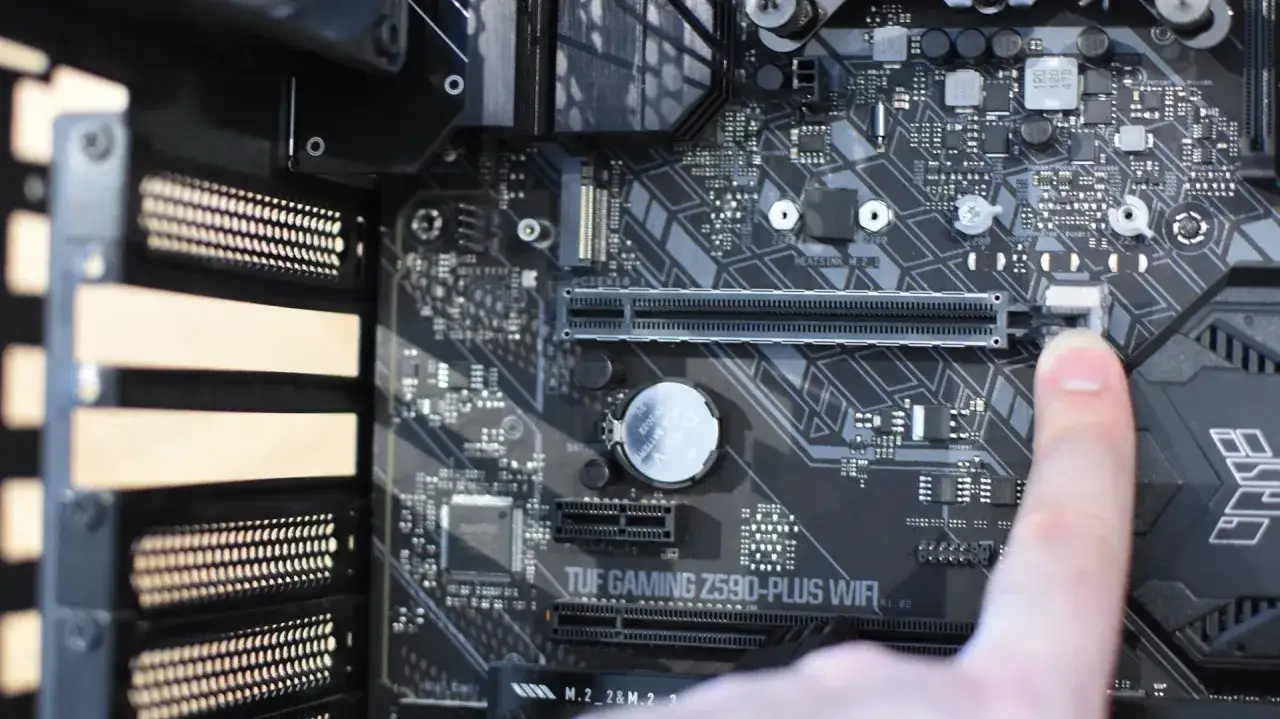 Doigt appuyant sur le loquet d'une carte mère TUF GAMING Z590-PLUS WIFI, prêt à installer une carte graphique.