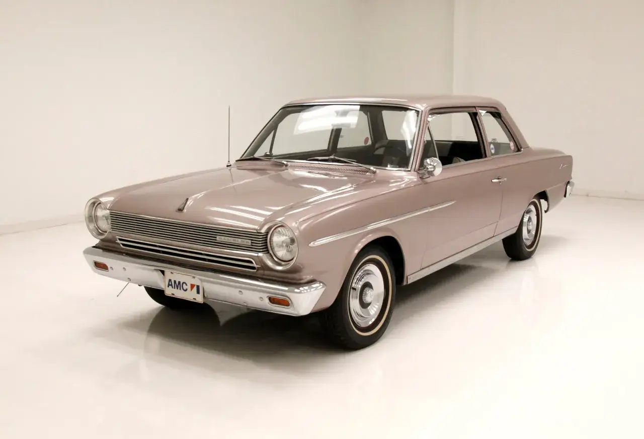En ljusrosa AMC Rambler fr&aring;n 1960-talet, en klassisk bland rambler bilmodeller, st&aring;r i ett studio.