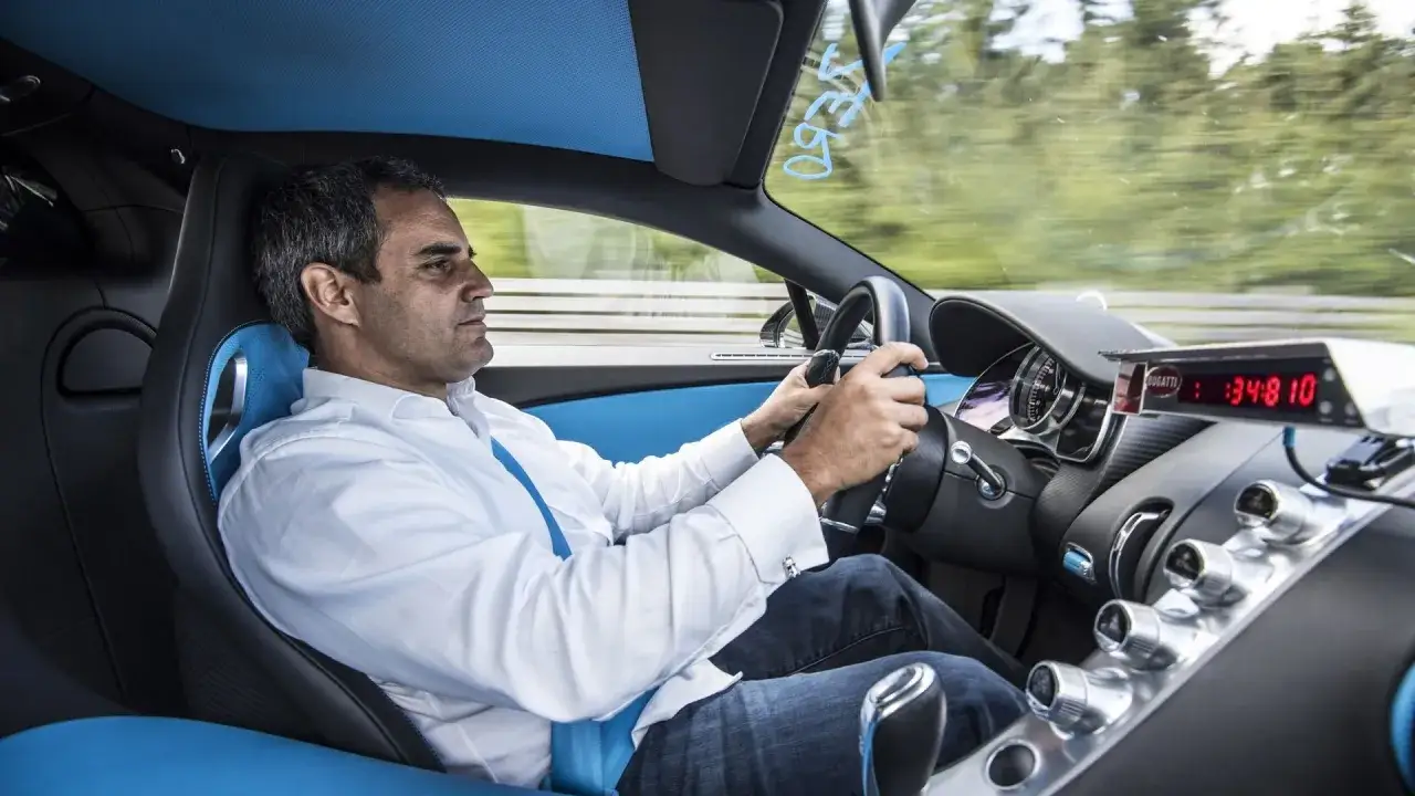 Un homme au volant d'une Bugatti Chiron, prêt à tester sa vitesse max. L'habitacle bleu et noir est luxueux.