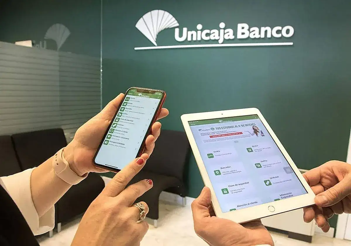 Manos sostienen un móvil y una tablet mostrando la app de Unicaja Banco, ideal para consultar reseñas y gestiones.
