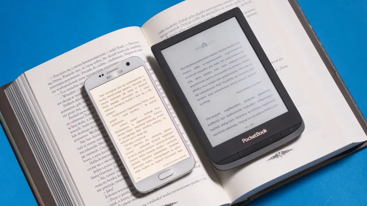 Smartfon i czytnik **epub** obok otwartej książki. Nowoczesność kontra tradycja w świecie literatury.