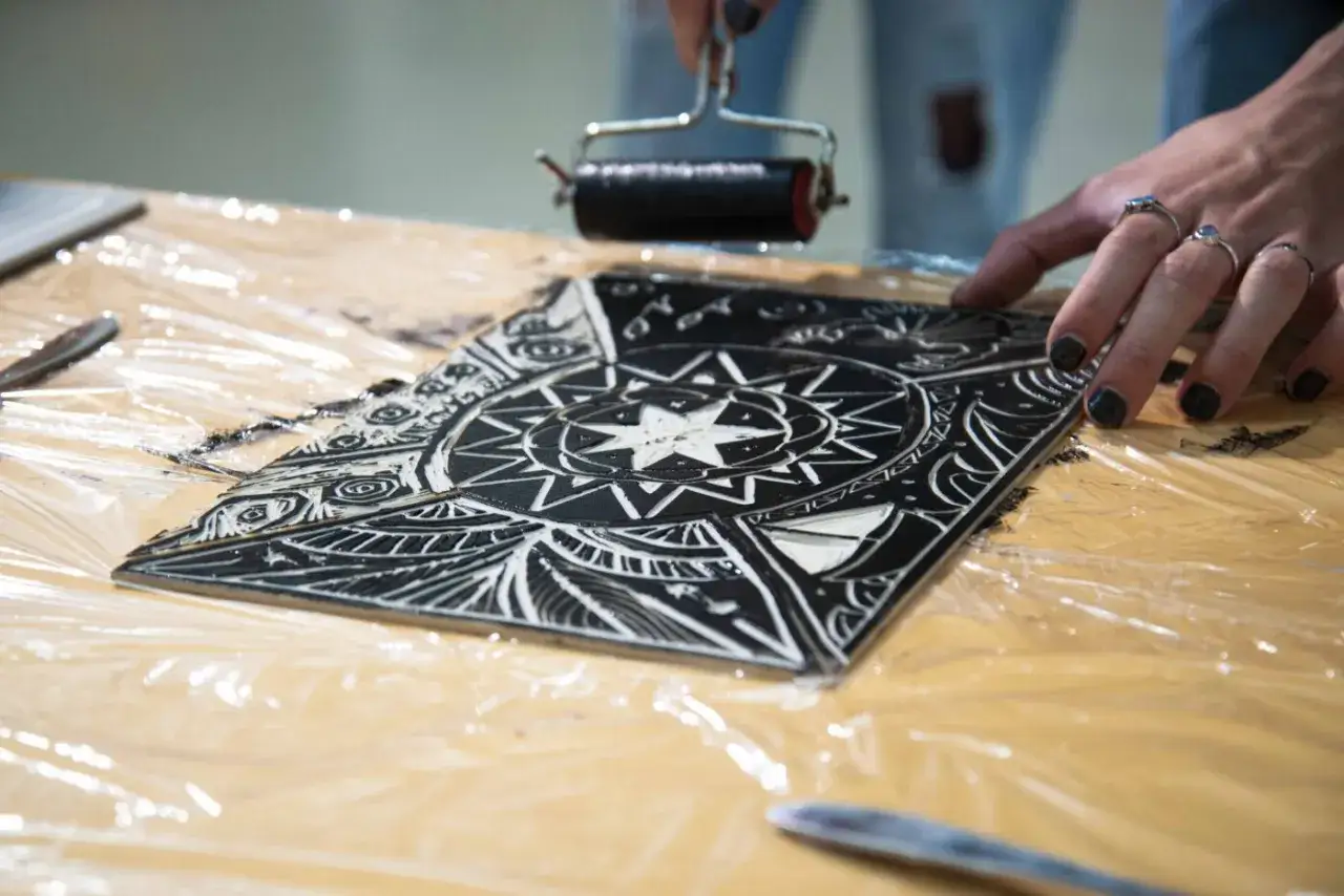 Application d'encre sur une plaque gravée, montrant les différents types de gravure. Une main prépare l'estampe.