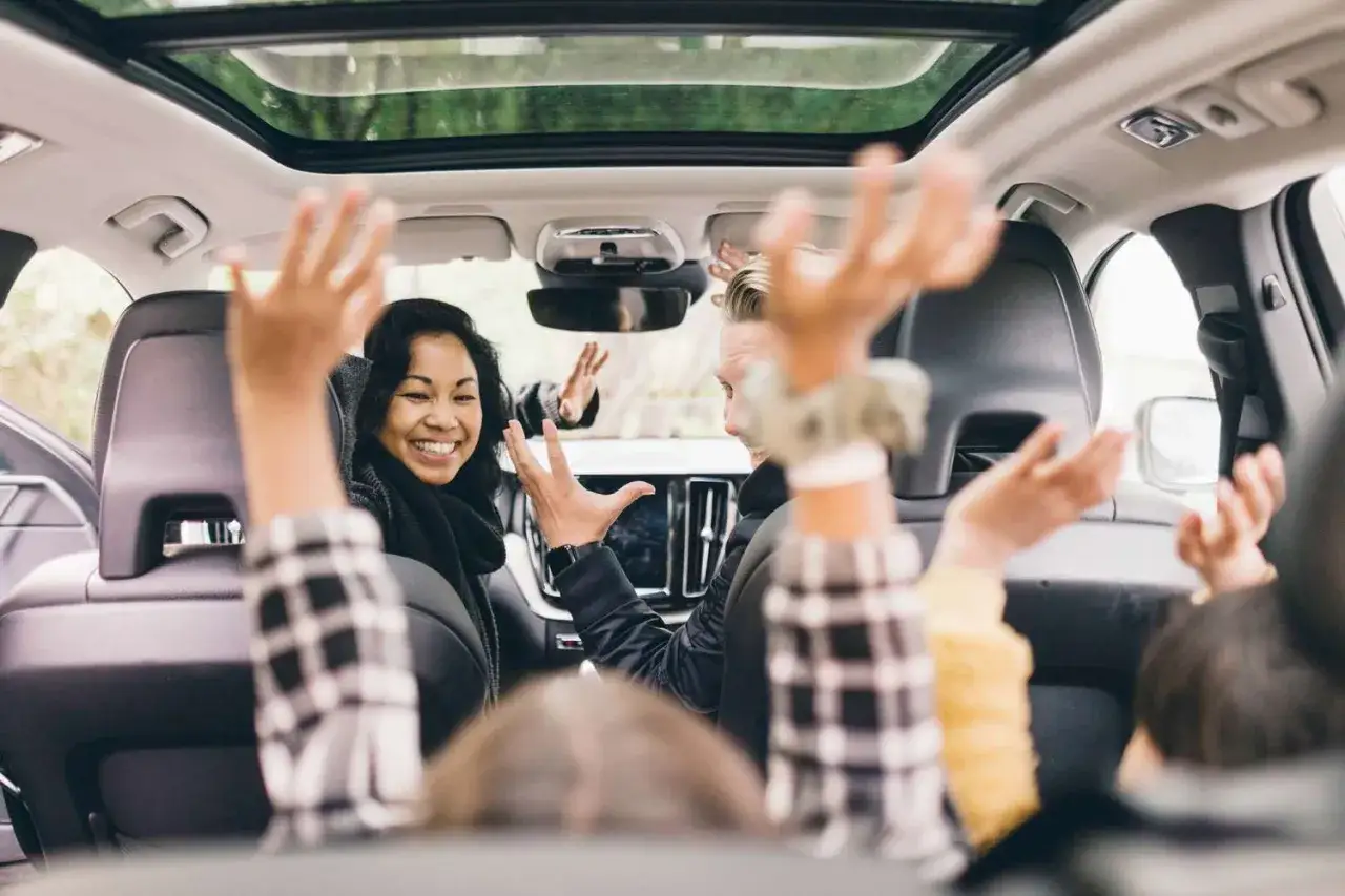 Fröhliche Menschen im Auto, die ihre Hände heben. Sie scheinen Spaß zu haben und spielen autofahrt spiele.