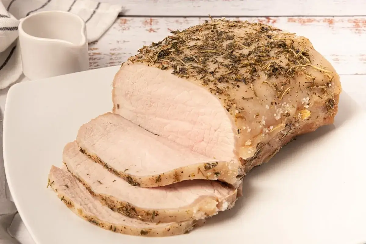 Lomo a la sal jugoso y tierno, cubierto de hierbas arom&aacute;ticas, servido en una fuente blanca con unas rodajas ya cortadas.