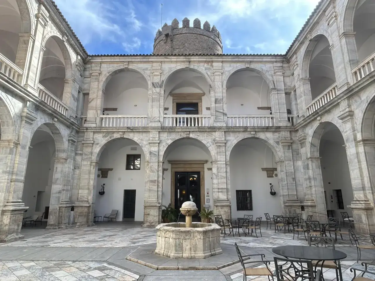 Patio con fuente y arcos de mármol, ideal para descubrir qué ver cerca de Zafra. Torres medievales coronan el edificio.