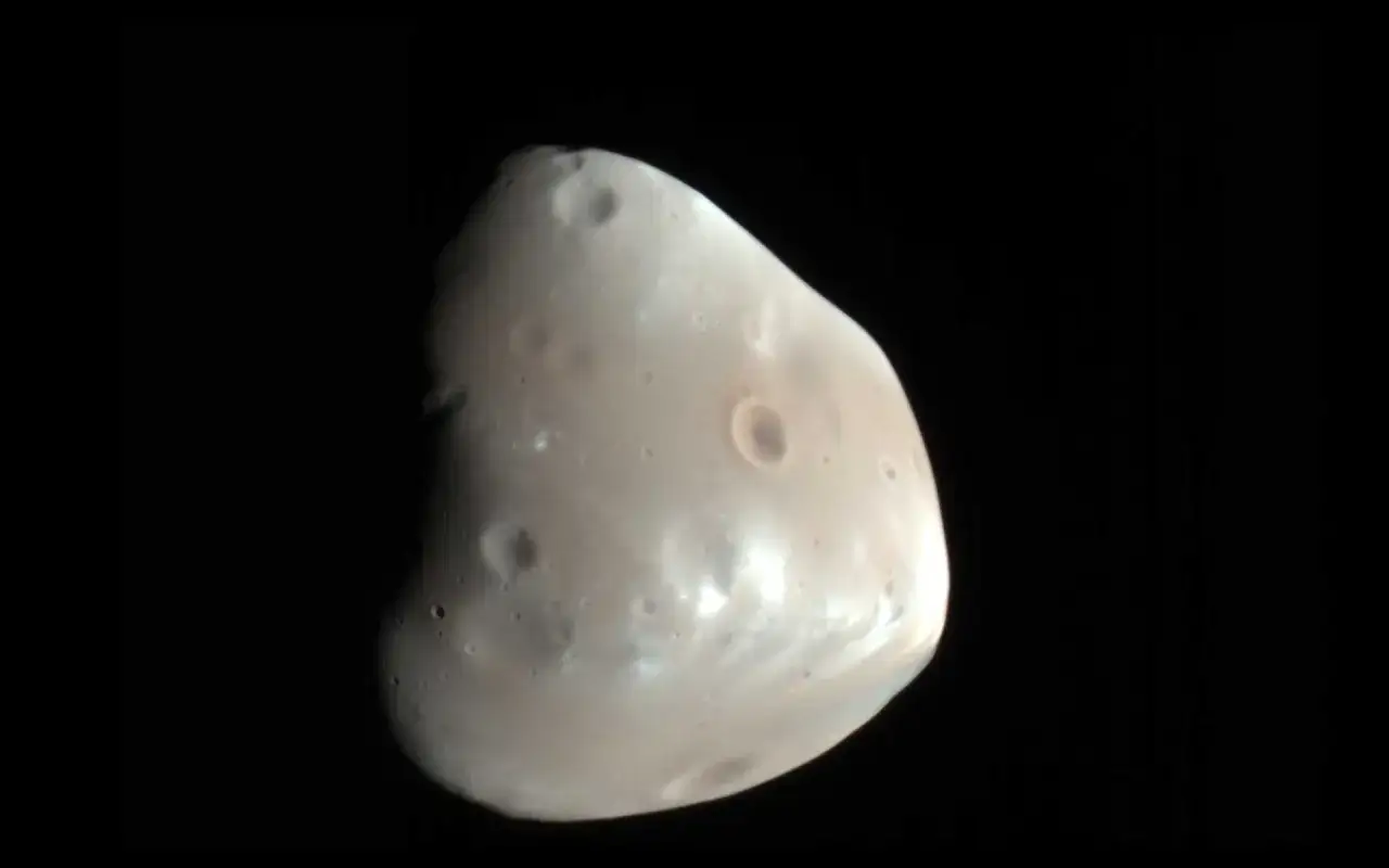 Deimos, jeden z księżyców Marsa, z licznymi kraterami na swojej nieregularnej powierzchni, unoszący się w czerni kosmosu.