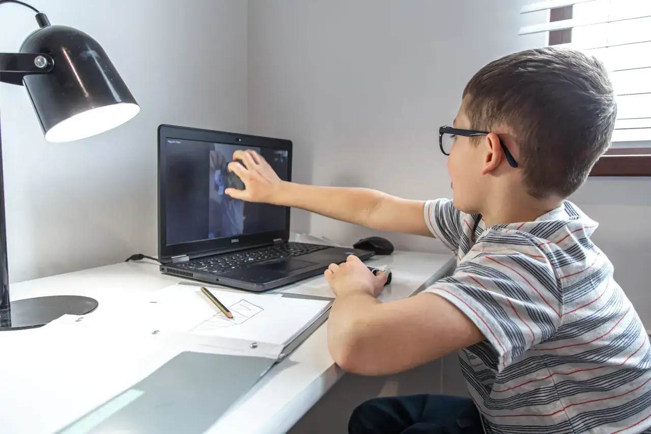 Ni&ntilde;o con gafas interact&uacute;a con videos educativos para ni&ntilde;os de 10 a 12 a&ntilde;os en su port&aacute;til.