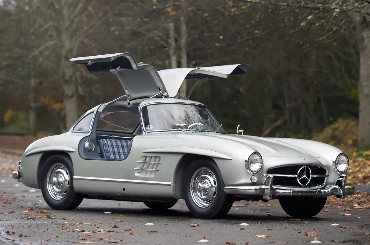 Silver Mercedes-Benz 300 SL Gullwing, en ikonisk måsvinge bil, står parkerad utomhus med dörrarna uppfällda.
