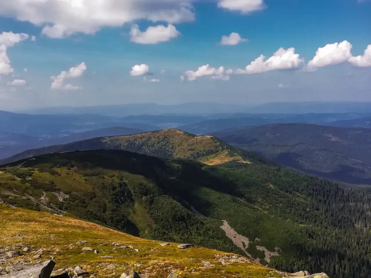 Malownicze pasmo g&oacute;rskie Beskid Żywiecki w słoneczny dzień. Zielone zbocza, skaliste fragmenty i błękitne niebo z białymi chmurami.