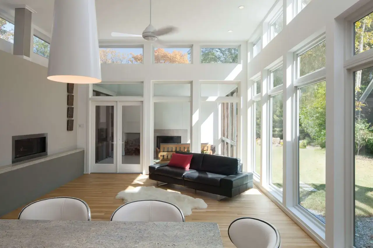 Sunlight streams through floor-to-ceiling windows, illuminating a modern living room. This is how to brighten a dark room, with natural light and minimalist decor.