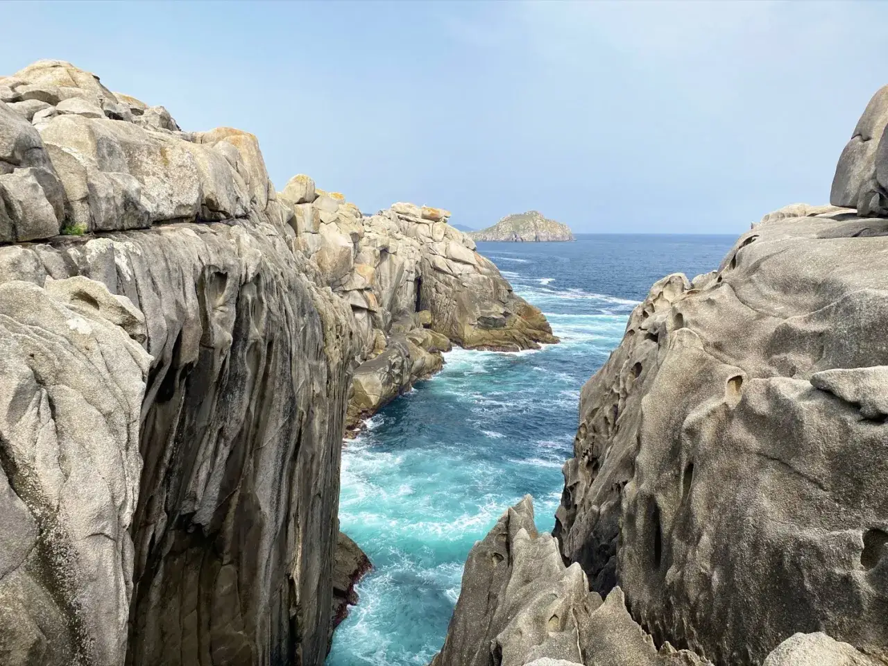 Majestuosos acantilados de papel Xove se alzan sobre aguas turquesas, con una isla solitaria en el horizonte.