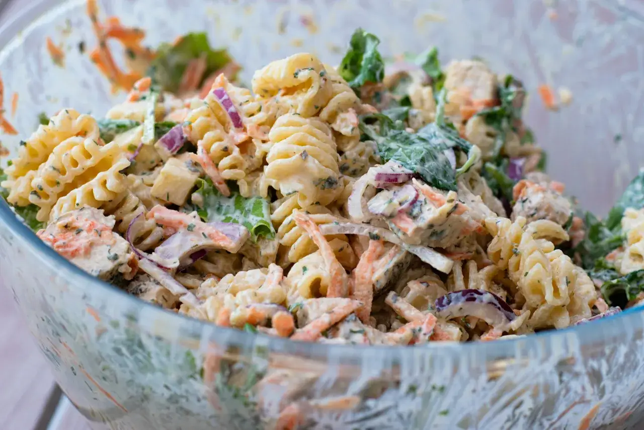 En stor skål med krämig pastasallad med kyckling, morötter, rödlök och gröna blad. Perfekt för en somrig picknick!