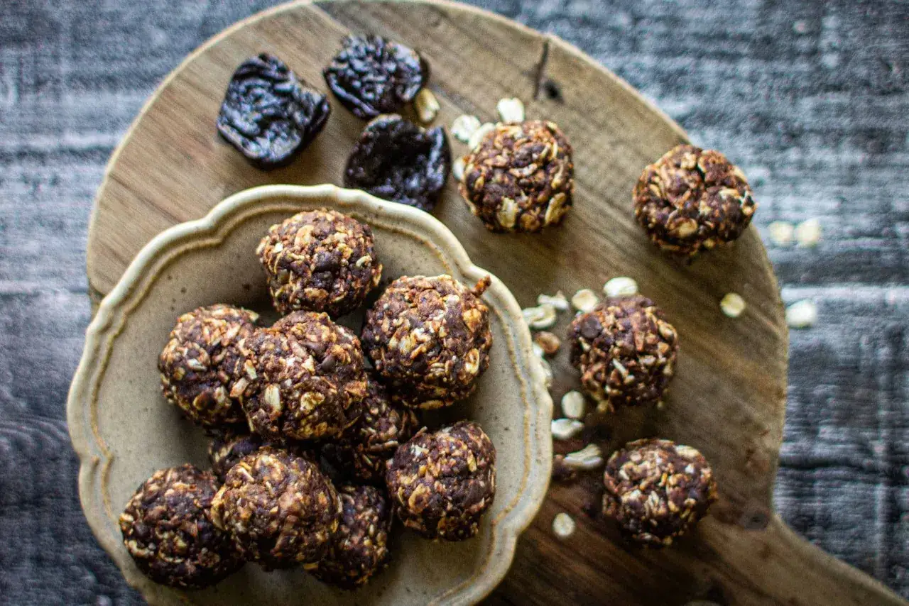 Schoko energy balls mit Haferflocken und Nüssen, daneben getrocknete Pflaumen. Ein gesunder Snack für zwischendurch.