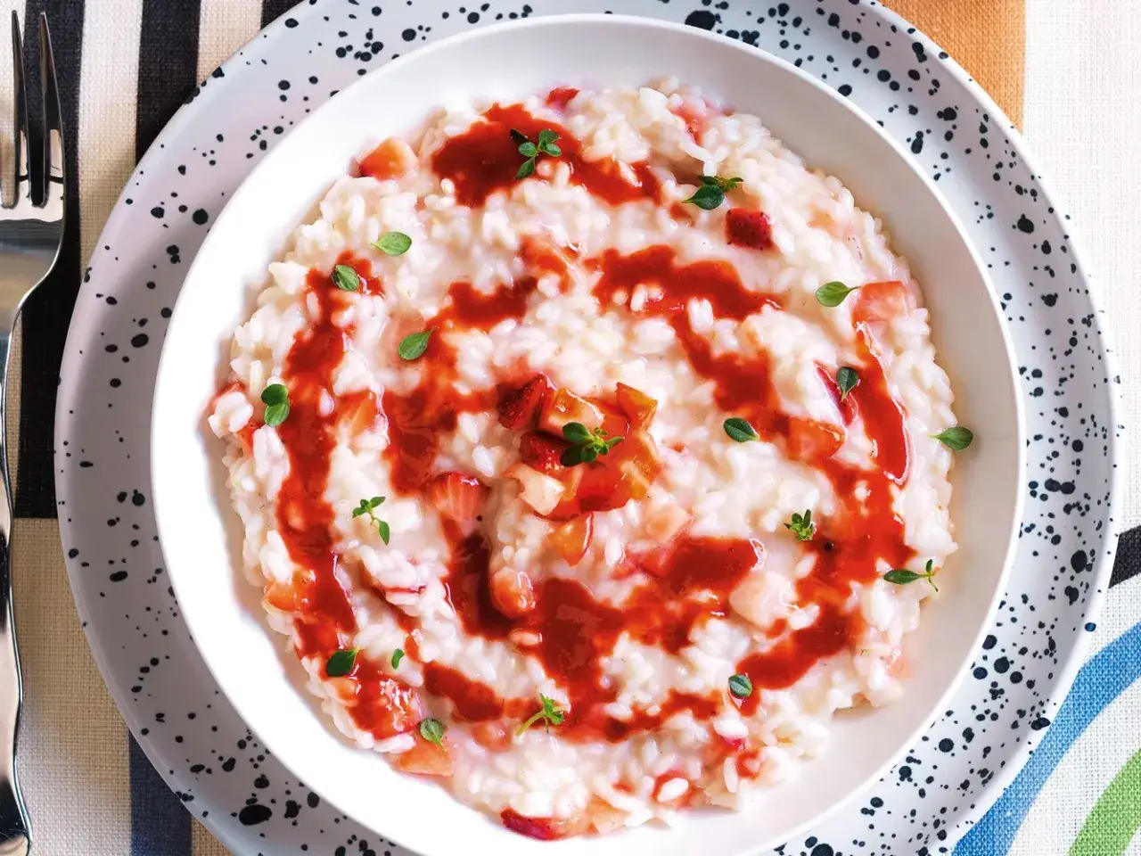 Un cremoso risotto alle fragole, guarnito con salsa di fragole e timo fresco, pronto per essere gustato.