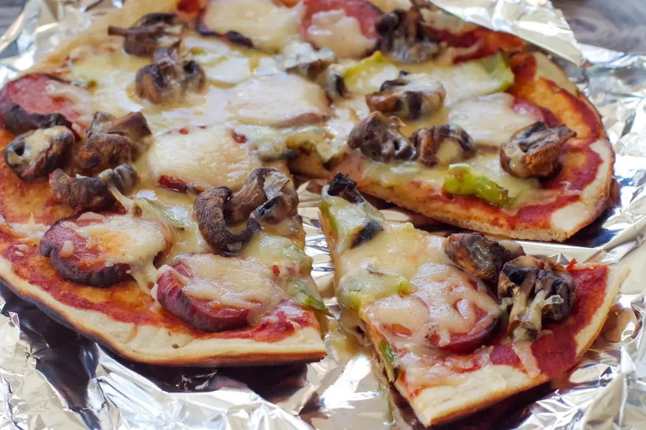 Delicious grilled pizza ideas: a savory pizza with mushrooms, sausage, and melted cheese on foil.