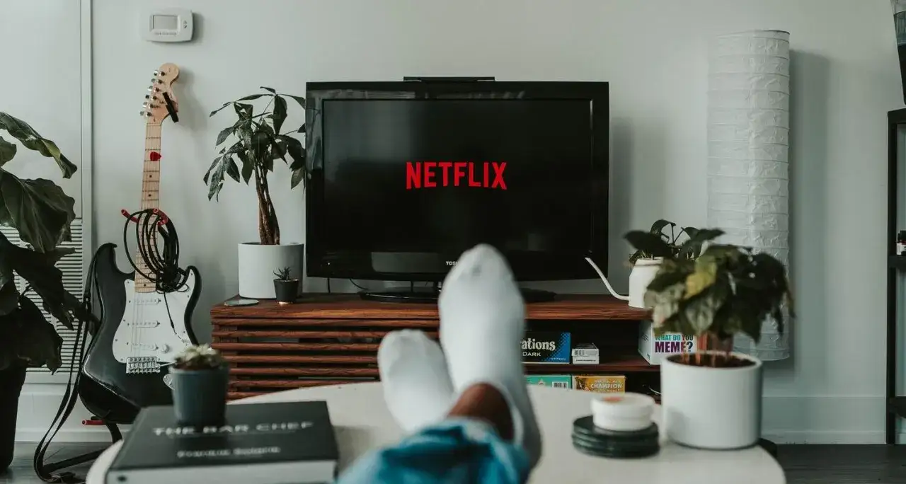 Relaks przy Netflixie, idealny dobry film na wieczór. Wygodnie rozłożone nogi, gitara w tle i rośliny tworzą przytulną atmosferę.