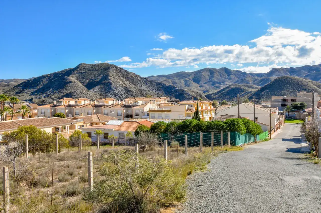 Pueblo de **los Lobos, Almería**, con casas blancas y tejados naranjas, rodeado de montañas áridas bajo un cielo azul con nubes.