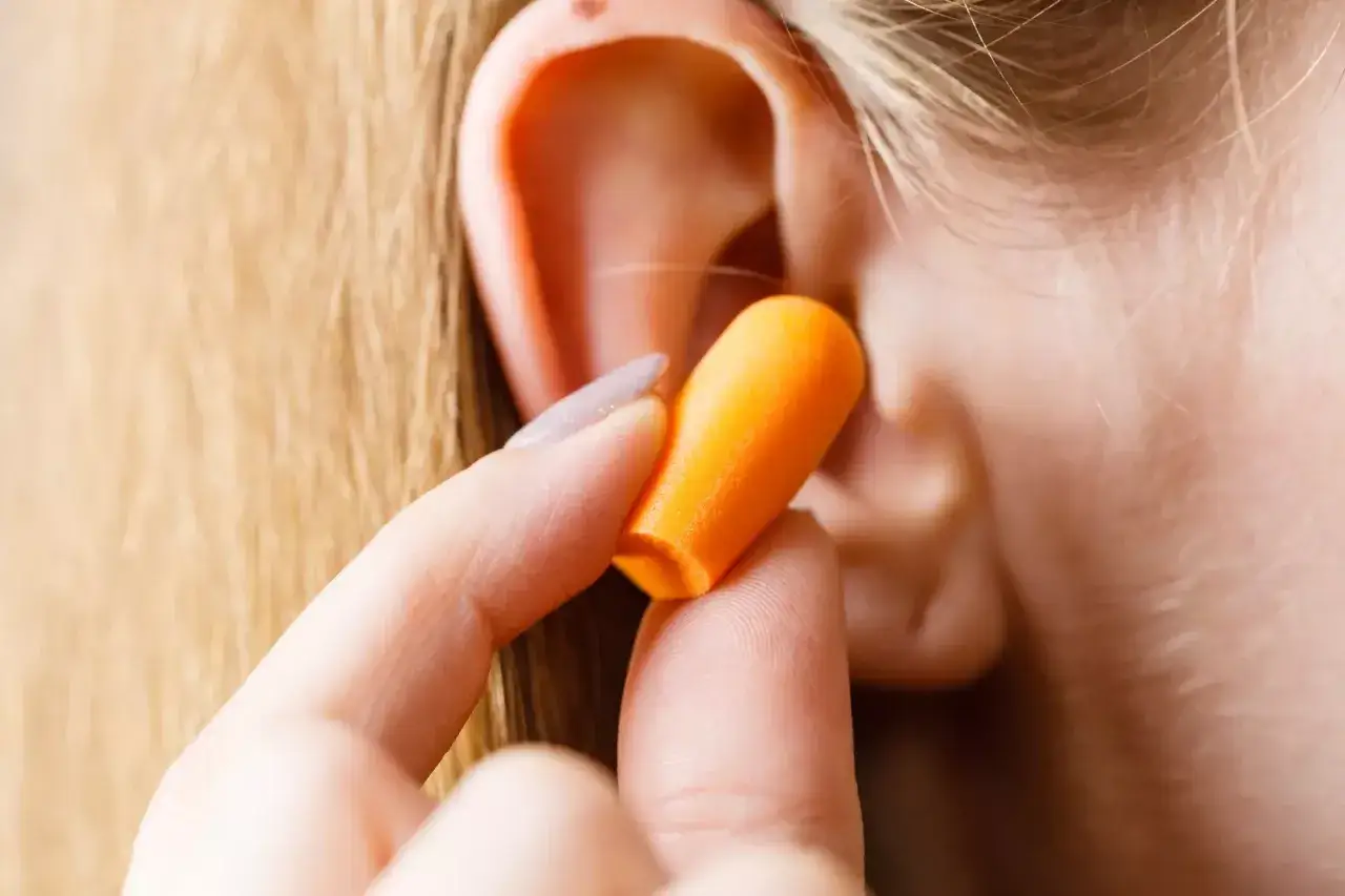 Main d'une personne ins&eacute;rant un bouchon d'oreille orange pour soulager l'hyperacousie.