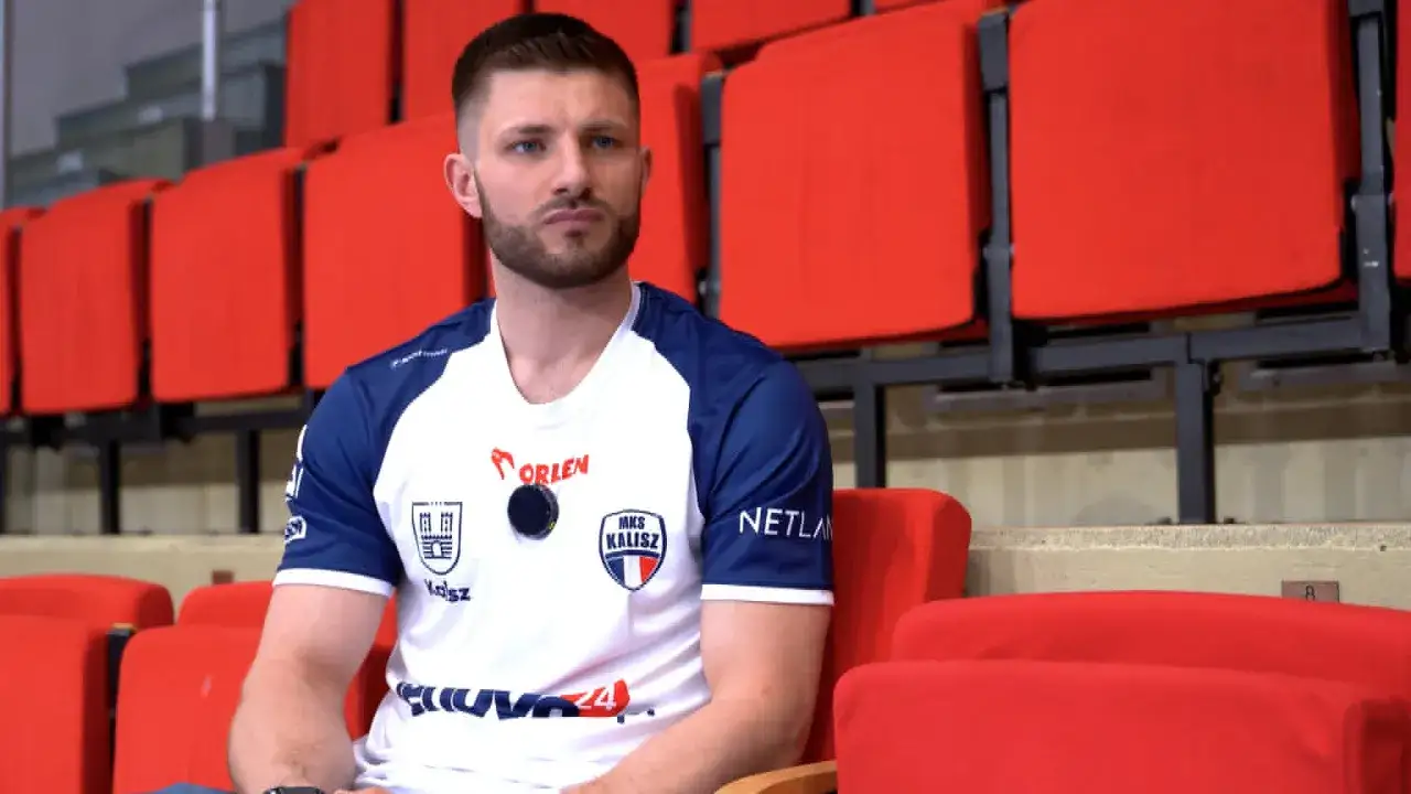 Marcel Sroczyk w koszulce MKS Kalisz siedzi na czerwonych trybunach.